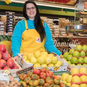 Smiling woman in a fruit market in Madrid, surrounded by fresh produce.